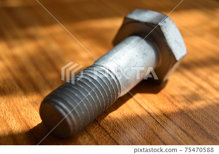 Galvanized metal with metric bolt, isolated on brown walnut wood Galvanized metal with metric bolt, isolated on brown walnut wood 75470588