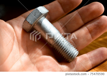 Galvanized metal with metric bolt and hand, isolated on brown walnut wood 75470590