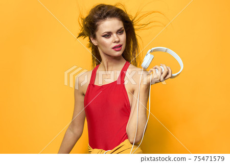 Cheerful woman in headphones listens to music in a red T-shirt yellow background Cheerful woman in headphones listens to music in a red T-shirt yellow background 75471579