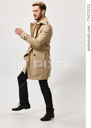 a man in trousers and a beige coat runs to the side on a light background a man in trousers and a beige coat runs to the side on a light background 75472312