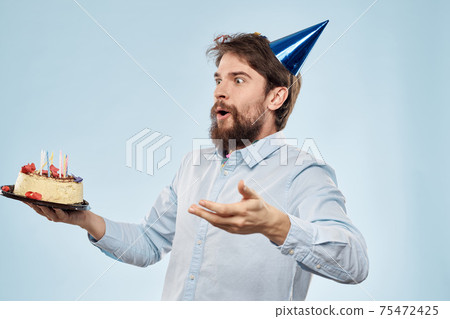Man with a plate of cake and a festive candle blue background cap corporate party Man with a plate of cake and a festive candle blue background cap corporate party 75472425