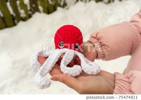Beautiful girl with a knitted octopus toy in her hands on the street in winter, red color 75474811