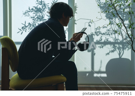 一個男人坐在一起的手機和耳機的輪廓 一個男人坐在一起的手機和耳機的輪廓 75475911