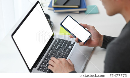 Cropped shot of man freelancer working with laptop computer and using smart phone. Cropped shot of man freelancer working with laptop computer and using smart phone. 75477773