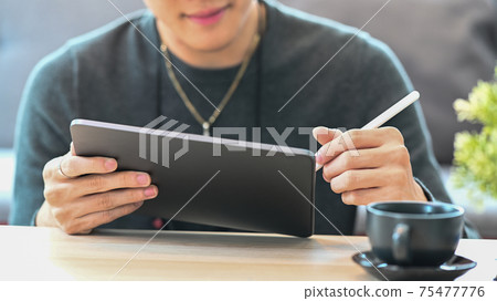 Cropped shot of smiling young man holding stylus pen writing on screen of digital tablet. Cropped shot of smiling young man holding stylus pen writing on screen of digital tablet. 75477776