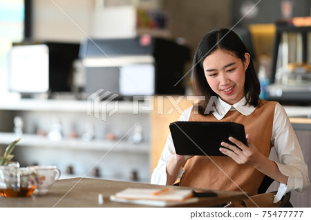 Happy young woman using digital tablet and sitting in coffee shop. Happy young woman using digital tablet and sitting in coffee shop. 75477777
