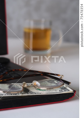 Glasses and dollar bills on the laptop keyboard against the background of a glass of tea with lemon, remote work, work on the Internet, freelancer Glasses and dollar bills on the laptop keyboard against the background of a glass of tea with lemon, remote work, work on the Internet, freelancer 75478354