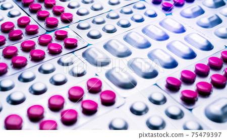 Pink tablets piils in blister pack and silver aluminium foil pack of pills. Pharmaceutical industry. Pharmaceutical manufacturing production. Round pink tablets pills and light resistant packaging. 75479397