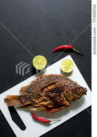Fried fish on white chopping block with black background Fried fish on white chopping block with black background 75480058