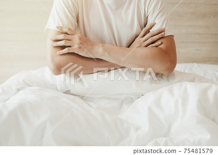 A man sitting on the bed and crossed arms on white bed in bedroom with and sunlight. A man sitting on the bed and crossed arms on white bed in bedroom with and sunlight. 75481579