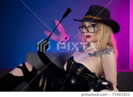 sexy woman in a corset and torn pants on the couch with a whip and a teddy bear in bdsm accessories 75481932