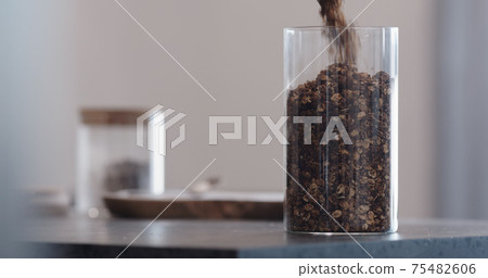 man chocolate granola pour into glass beaker jar on concrete countertop 75482606