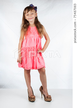 Cute little girl in high-heeled shoes posing on a white background. 75487083