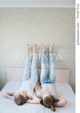 Young attractive heterosexual couple man and woman lie on the bed in the bedroom dressed in casual clothes. Weekend rest in bed is a good time 75487312