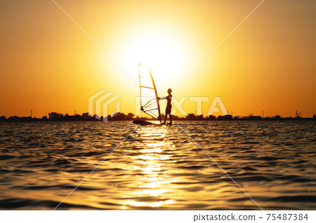 Woman windsurfer silhouette at lake sunset. Beautiful beach landscape. Summer water sports activities, recreation and travel concept 75487384