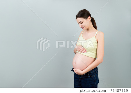 pregnant woman in unzipped jeans showing her naked belly at colorful background with copy space. Baby expecting concept 75487519