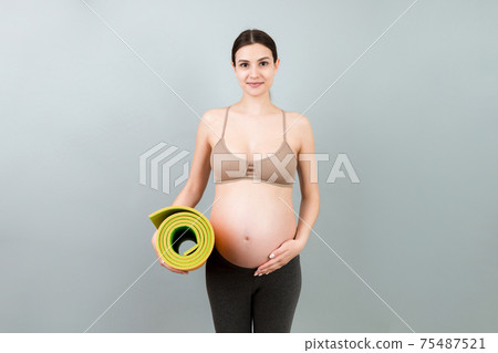 Pregnant Girl Holding Yoga Mat Standing Over Colored Background. Studio Shot, Free Space For Design 75487521