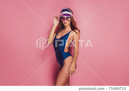 Woman in plastic cap visor and swimwear on pink 75489718