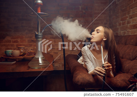 Young woman lying on sofa and smokes hookah in bar Young woman lying on sofa and smokes hookah in bar 75491607