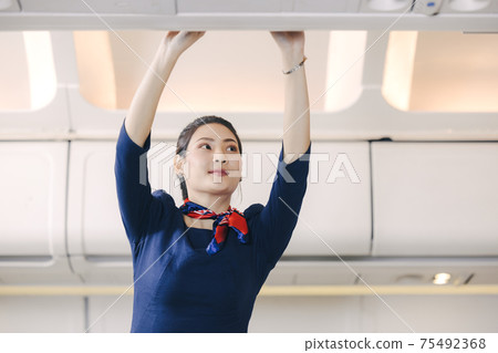 The stewardess helps the passengers to put their luggage in the cabin of the plane. Stewardess in the airplane. 75492368