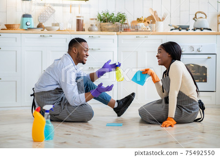 Cheerful black couple chatting to each other on kitchen floor after domestic cleanup, full length portrait Cheerful black couple chatting to each other on kitchen floor after domestic cleanup, full length portrait 75492550