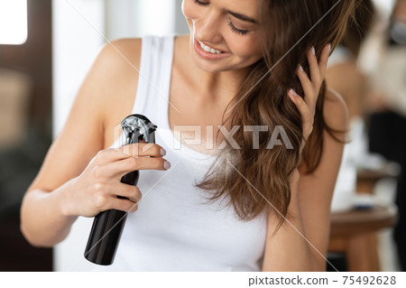 Happy Woman Spraying Hairspray Styling Wavy Hair In Bathroom, Cropped 75492628