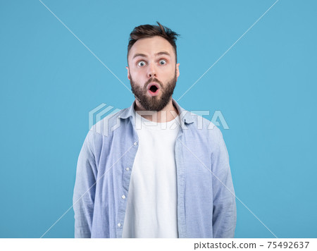 Portrait of stunned young guy opening mouth in shock on blue studio background Portrait of stunned young guy opening mouth in shock on blue studio background 75492637
