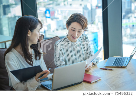 Two business women (casual) meeting while operating a computer in the office 75496332