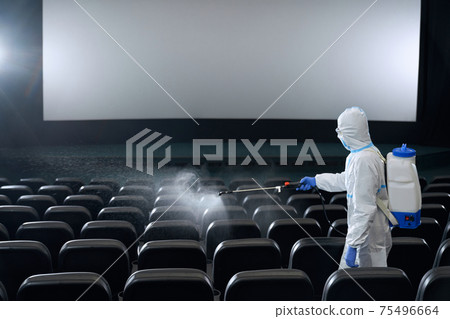 Worker cleaning seats in cinema hall with disinfectants. 75496664