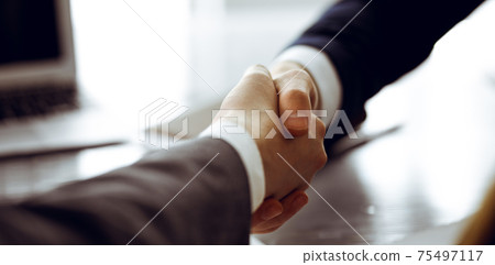 Unknown businessman shaking hands with his colleague or partner above the glass desk in modern office, close-up. Business people group at meeting 75497117
