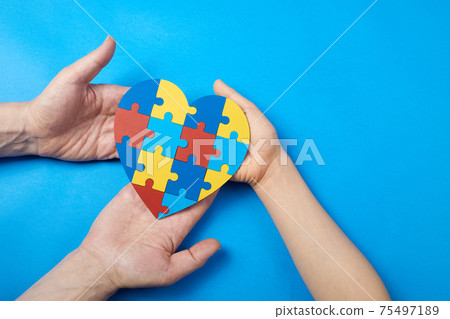 Father and autistic son hands holding jigsaw puzzle heart shape. Autism spectrum disorder family support concept. World Autism Awareness Day Father and autistic son hands holding jigsaw puzzle heart shape. Autism spectrum disorder family support concept. World Autism Awareness Day 75497189