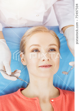 Happy smiling woman is being examined by dentist at dental clinic. Healthy teeth and medicine, stomatology concept Happy smiling woman is being examined by dentist at dental clinic. Healthy teeth and medicine, stomatology concept 75497504