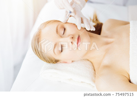 Beautician doctor doing beauty procedure with syringe to caucasian female face. Cosmetic medicine and surgery, beauty injections concept 75497515