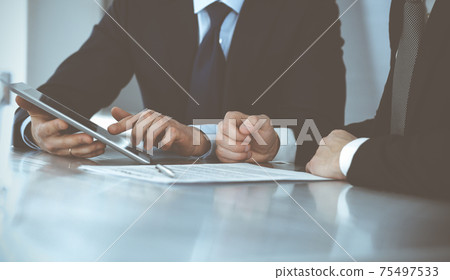 Business people using tablet computer while working together in modern office. Unknown businessman with colleague at workplace. Teamwork and partnership concept Business people using tablet computer while working together in modern office. Unknown businessman with colleague at workplace. Teamwork and partnership concept 75497533