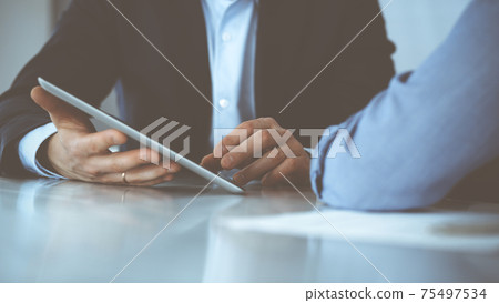 Business people using tablet computer while working together at the desk in modern office. Unknown businessman or male entrepreneur with colleague at workplace. Teamwork and partnership concept Business people using tablet computer while working together at the desk in modern office. Unknown businessman or male entrepreneur with colleague at workplace. Teamwork and partnership concept 75497534