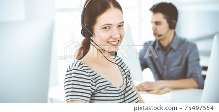 Casual dressed young woman using headset and computer while talking with customers online. Group of operators at work. Call center, business concept Casual dressed young woman using headset and computer while talking with customers online. Group of operators at work. Call center, business concept 75497554