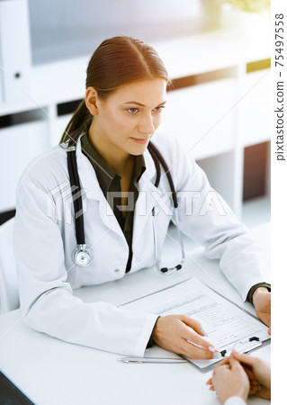 Woman-doctor and patient sitting and talking at sunny hospital office. Green color blouse suits to therapist. Medicine and healthcare concept Woman-doctor and patient sitting and talking at sunny hospital office. Green color blouse suits to therapist. Medicine and healthcare concept 75497558