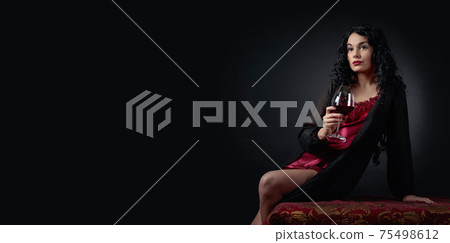 Portrait of attractive brunette with glass of red wine on a black background. 75498612