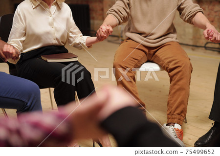 Several intercultural patients of psychological group holding by hands during session 75499652