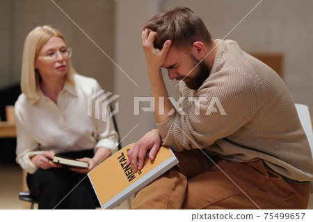 Young bearded male patient with psychological problem or trauma holding his head in hand 75499657