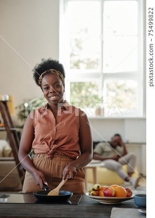 Young smiling woman of African ethnicity looking at you while standing by electric stove 75499822