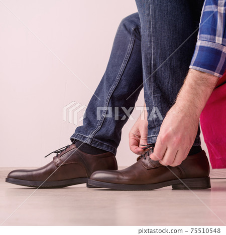 A man in a stylish brown shoes, tying laces is sitting on a red chair A man in a stylish brown shoes, tying laces is sitting on a red chair 75510548