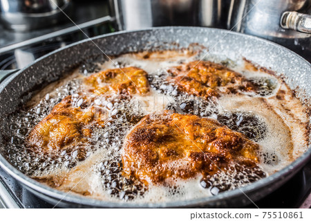 Schnitzels being fried in oil inside a dark pan 75510861