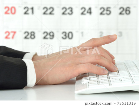Hands of a businessman working on a computer in front of a calendar 75511319