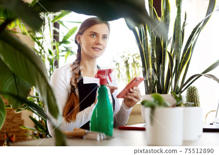 A florist girl uses her phone to take orders online at a flower shop. A florist girl uses her phone to take orders online at a flower shop. 75512890