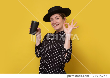 Caucasian woman in black hat holding coffee cup showing ok gesture 75515743