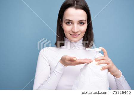 Young girl sanitizer in hands in the studio on a blue background. Hand disinfection and germ prevention. 75516440