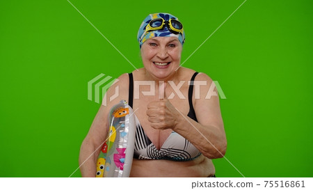 Senior woman tourist in swimsuit bra, swim goggles with swimming ring showing thumb up gesture 75516861