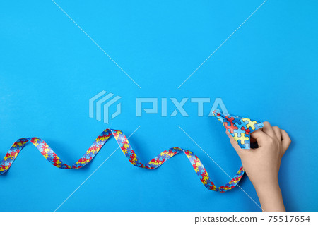 Autism awareness. Aitistic child hand holding paper plane in origami style with autism awareness ribbon on blue background. Autism awareness. Aitistic child hand holding paper plane in origami style with autism awareness ribbon on blue background. 75517654