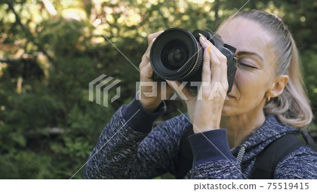 Traveler photographing scenic view in forest. One caucasian woman shooting close up look. Girl take photo video on dslr mirrorless camera. Traveler photographing scenic view in forest. One caucasian woman shooting close up look. Girl take photo video on dslr mirrorless camera. 75519415